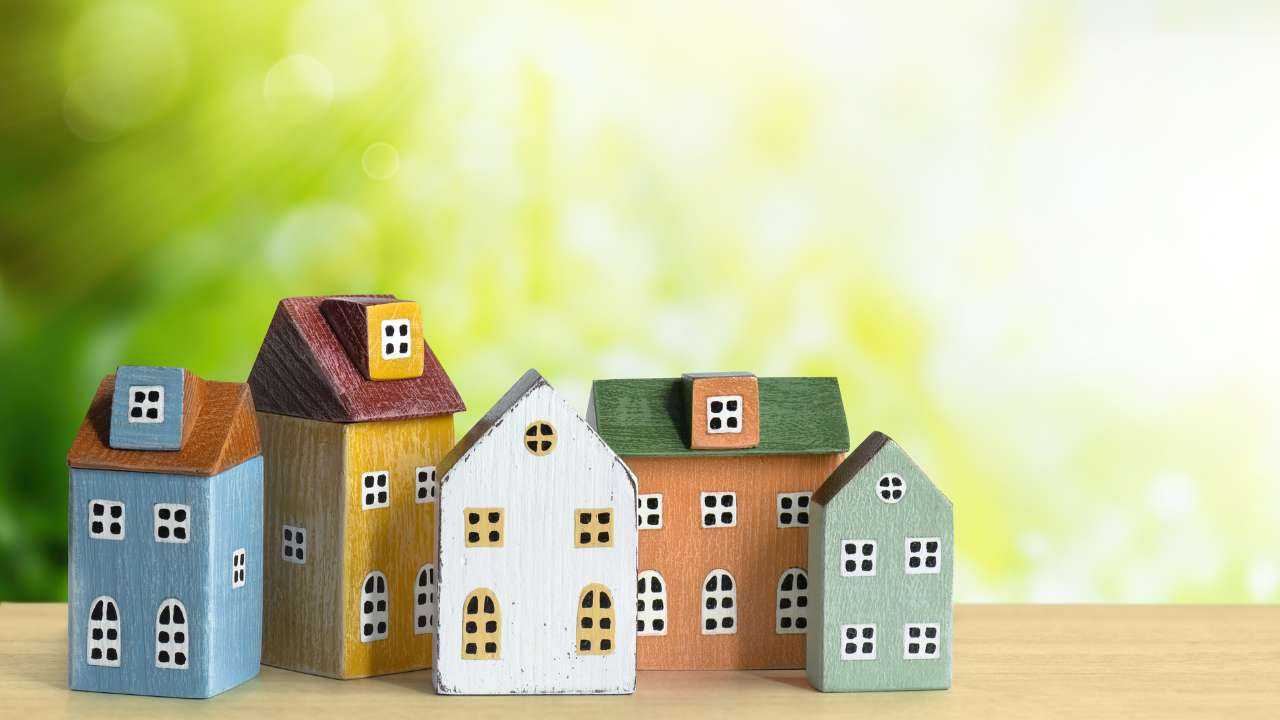 Пять миниатюрных и цветных домиков на фоне зелени как символ выгодной ипотеки с господдержкой