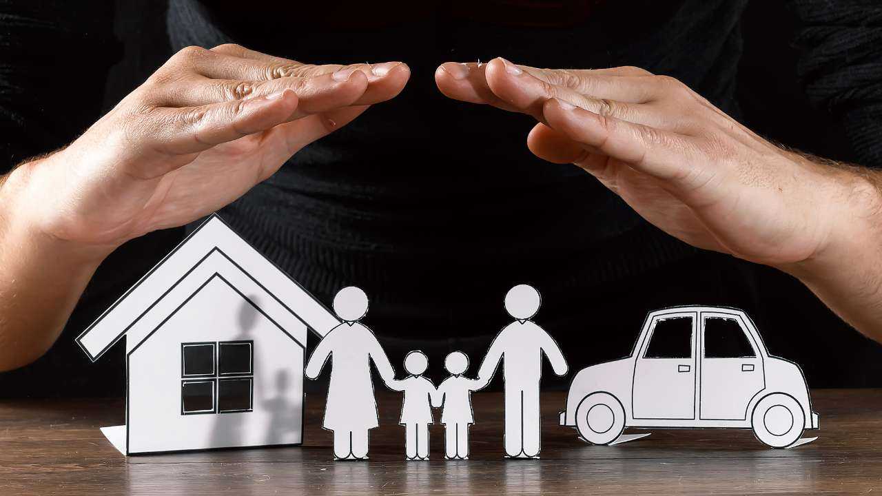 Защита дома и семьи с помощью страхования имущества, изображенная ладонями-домиком и бумажными фигурками