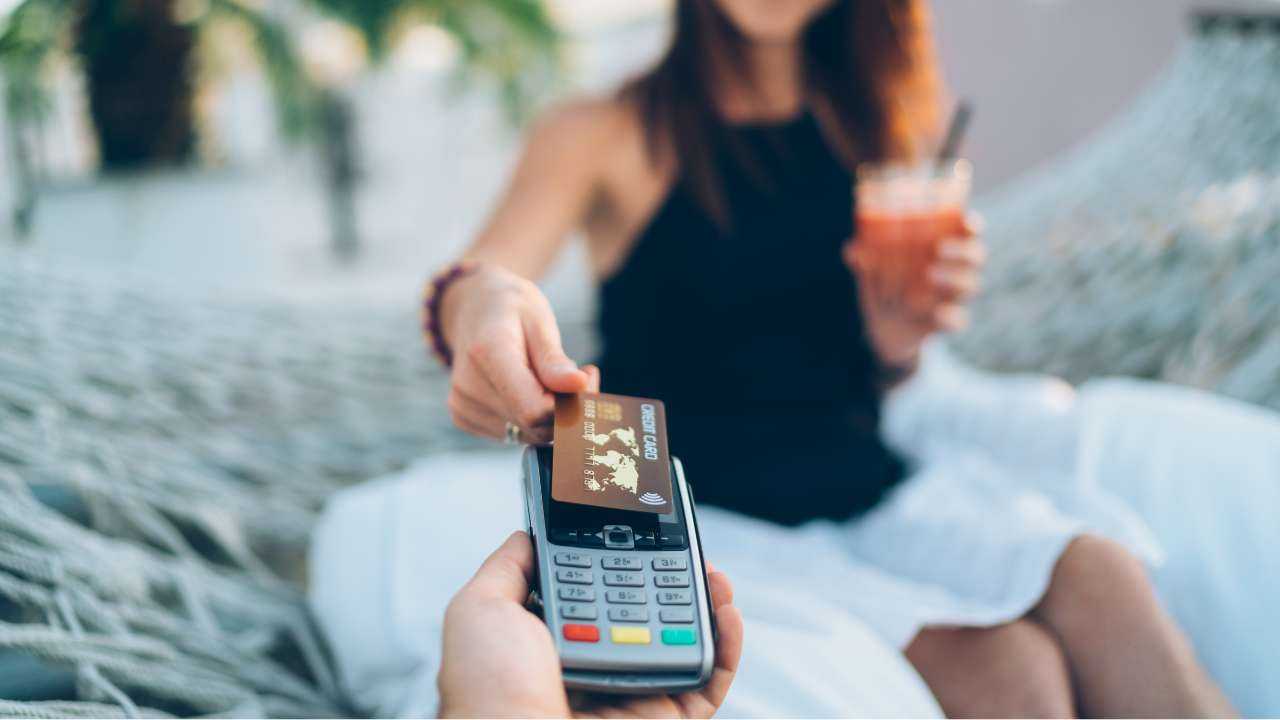 Девушка сиди на курорте, пьет коктейль и расплачивается банковской картой, на которую зачислены отпускные