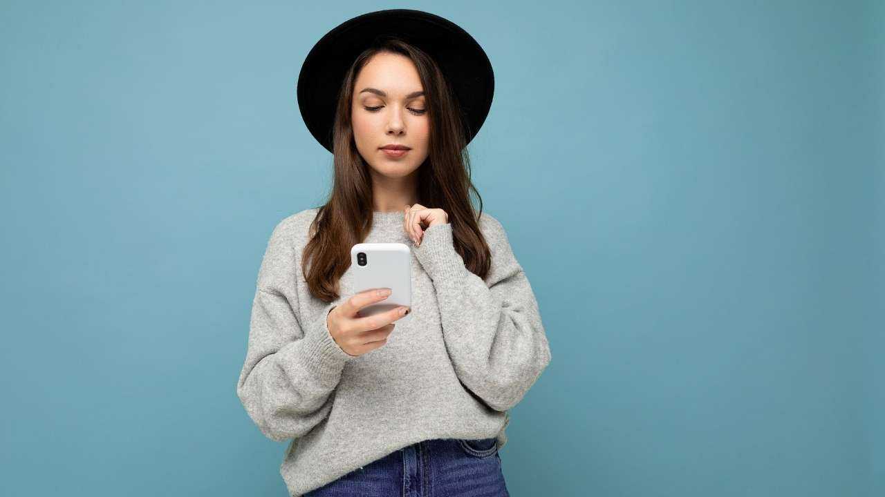 Девушка в шляпке ищет в смартфоне варианты займа денежных средств на карту